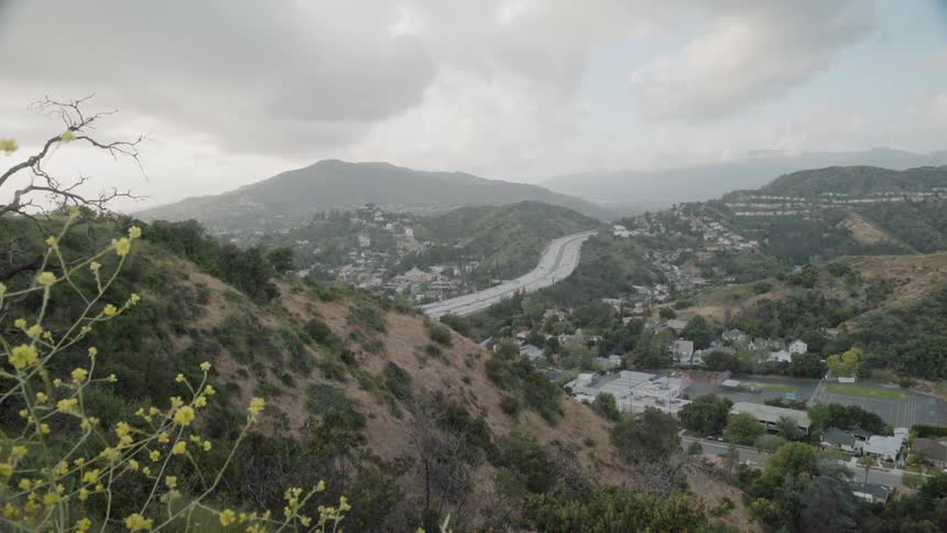 Traffic is flowing on a freeway in an hilly area in during daylight