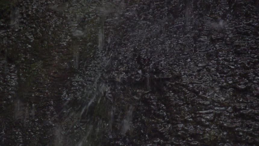 A close view of water splashing down onto a large, dark-colored stone