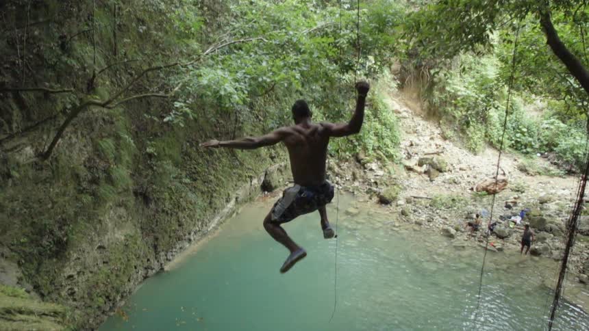 A man jumps off a cliff and into a lake in the woods