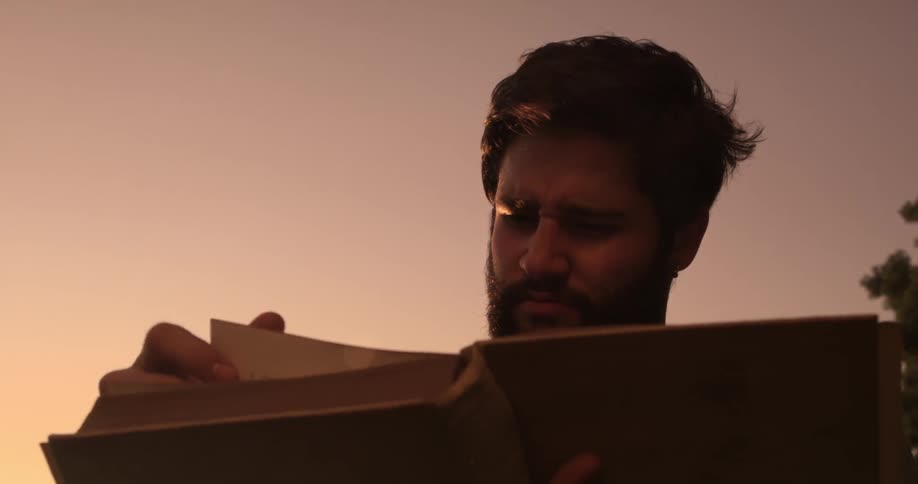 A bearded man flips through a large book outside