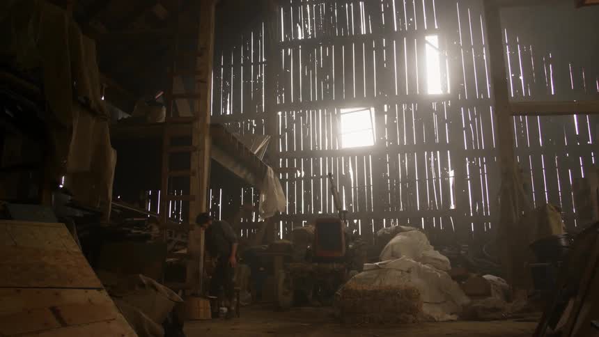 Man walking inside of a barn with light shining between the wall panels
