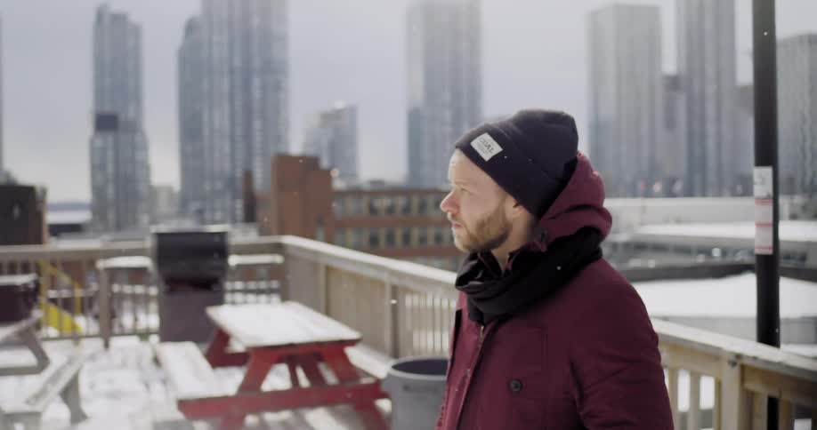 A man standing on a balcony as it snows in an urban area