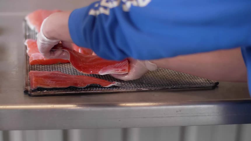A person is placing salmon filets onto a rack inside a kitchen in daylight