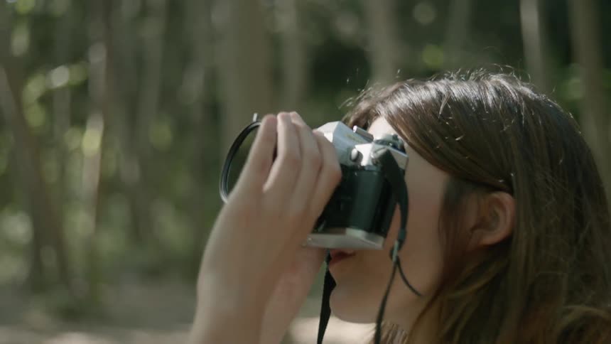 A woman is focusing her camera and taking a photo in a natural setting in daylight