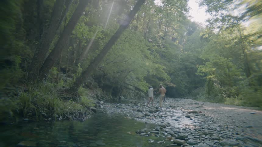 A man and woman walk on rocks in a stream