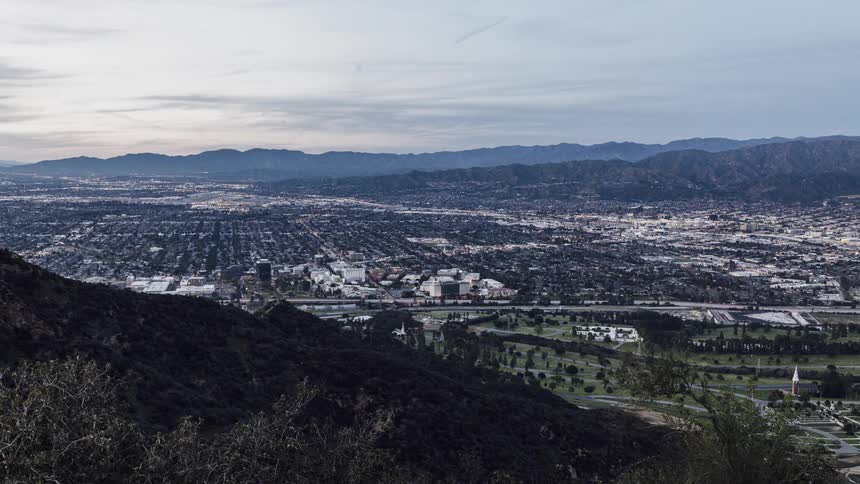 A hill overlooks roads and city as day turns to night