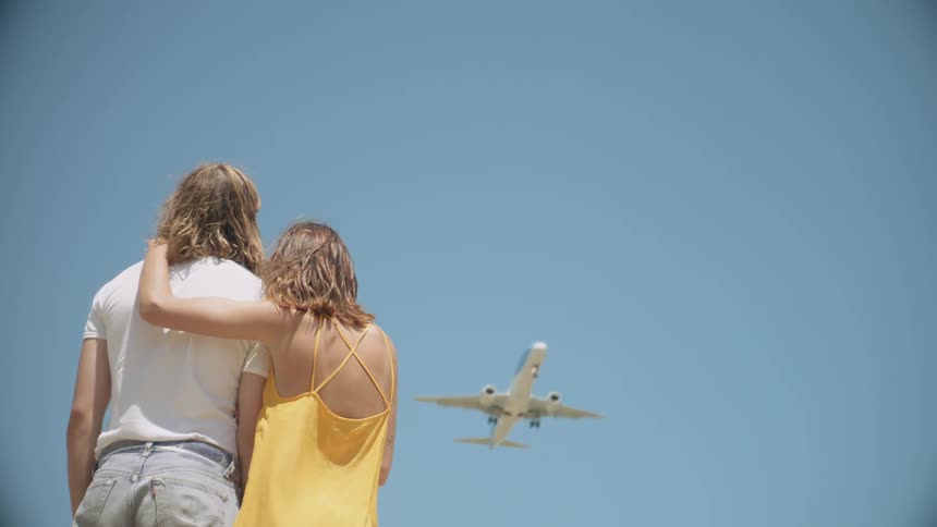 A man and woman watch an airplane fly overhead