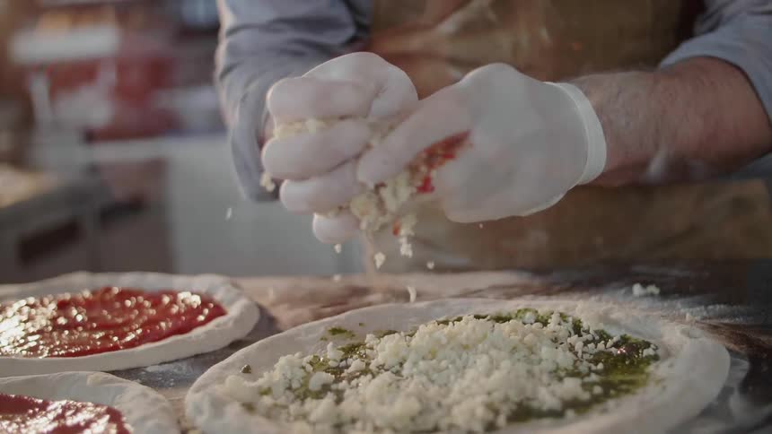 White gloved hands drop cheese onto a pizza
