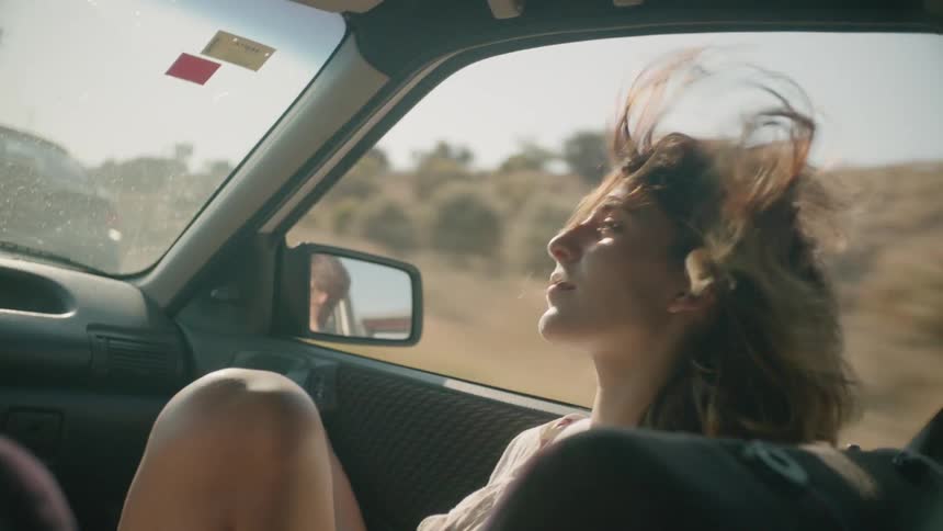 A woman's hair is being blown by the wind as she rides in a car in daylight