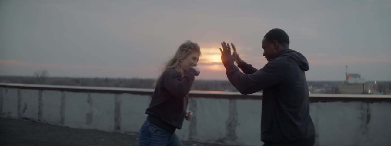 A woman is boxing a man's hands near the water