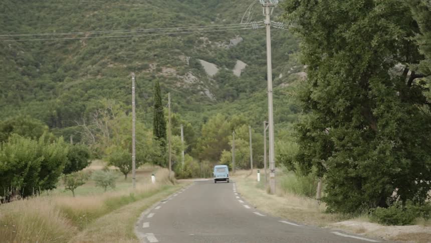 Blue vehicle drives on a country road turning left