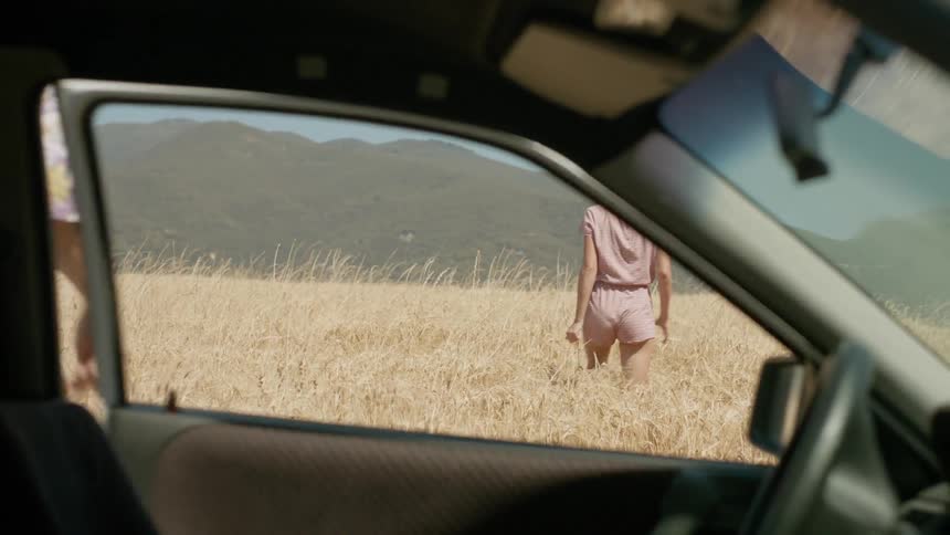 A man and woman walk in a grassy field near their parked car