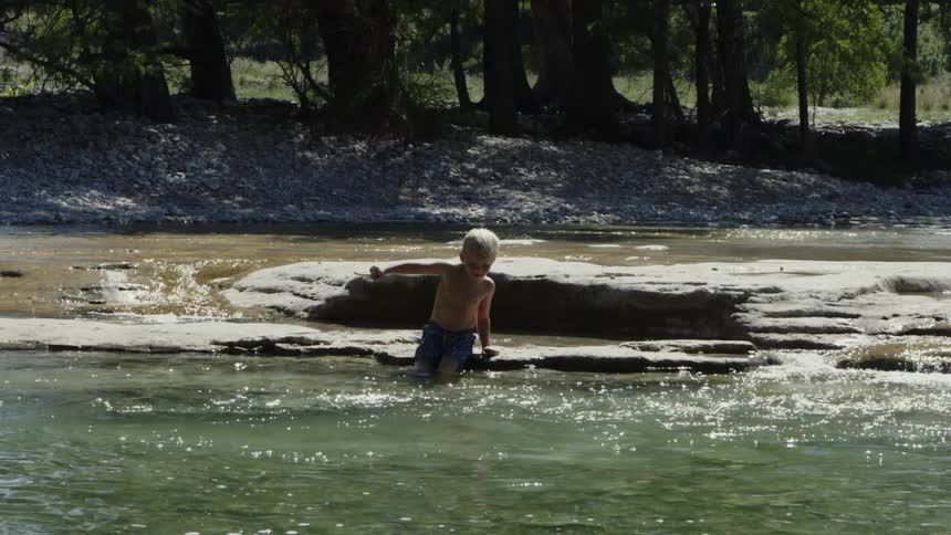 Young boy slides off a rock into the water