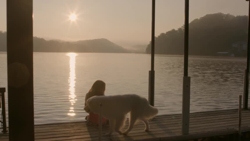 A furry white dog walks next to a girl on a dock