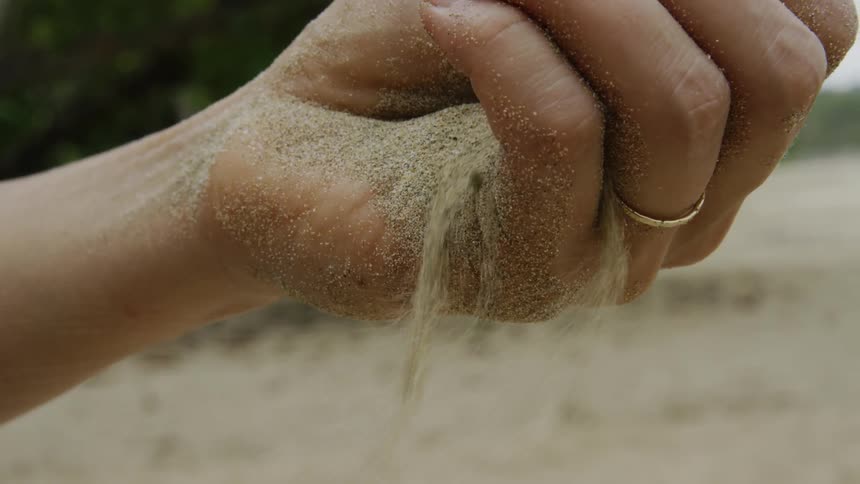 Sand sifts through a hand on a beach