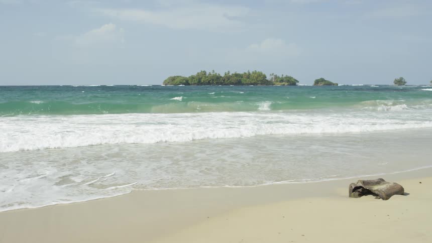 Frothy waves roll into the sandy beach under a blue sky