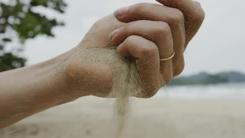Sand sifts through a woman's hand on a beach