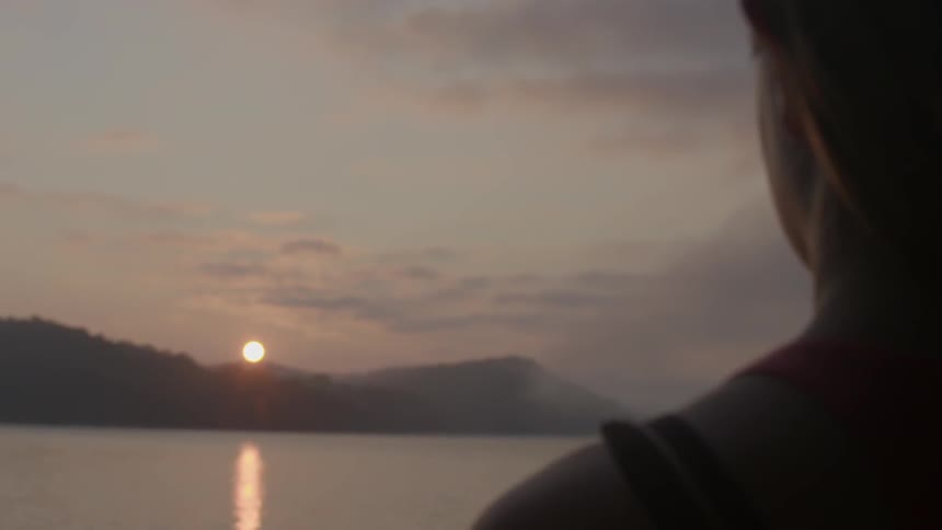 A woman looks over a lake at sunset