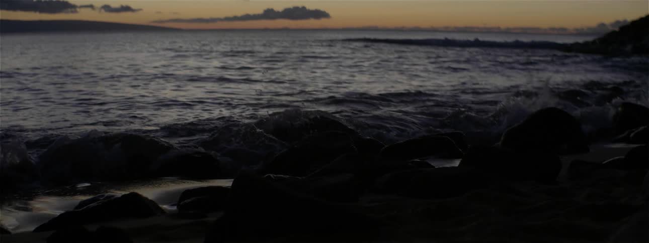 The sun is sitting on the beach as waves crash on the rocks