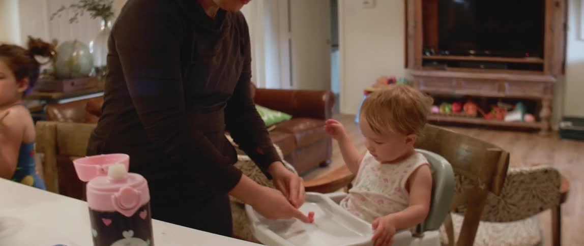 A mom breaks berries up and puts on the highchair tray for baby