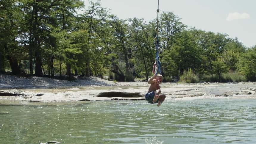 A boy swings on a rope and jumps into the river