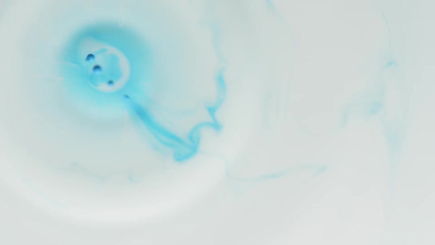 Drops of blue paint spread through white liquid