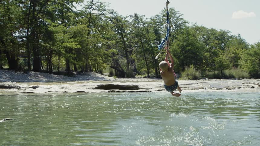A kid is using a zip line to cross a lake