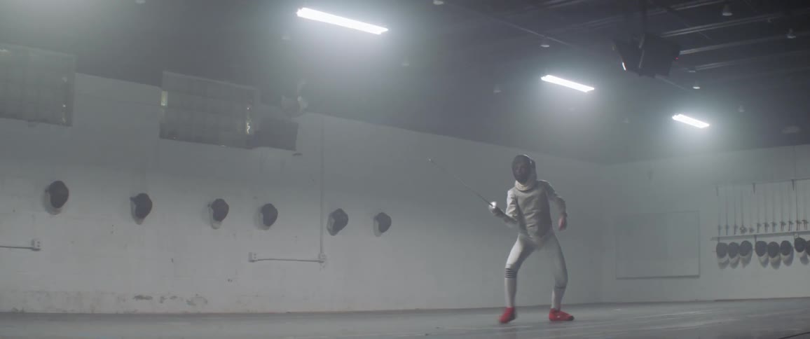 A person fences beneath fluorescent lights