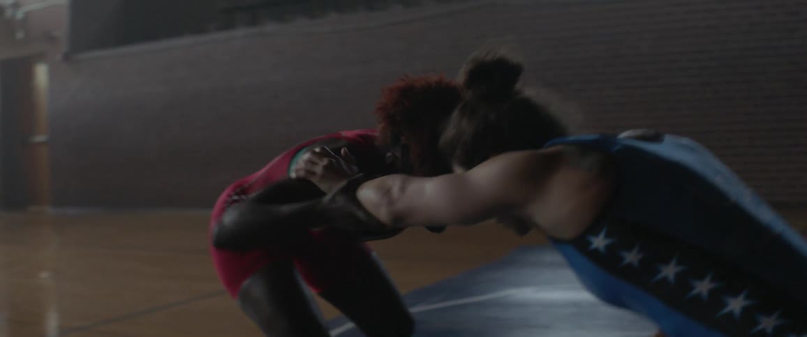 Two women wrestle on a large mat in the gym