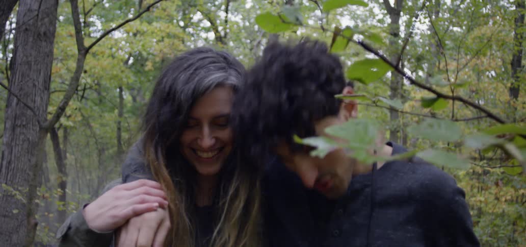 A man has his arm around a woman's shoulders as they are walking in a forest in daylight