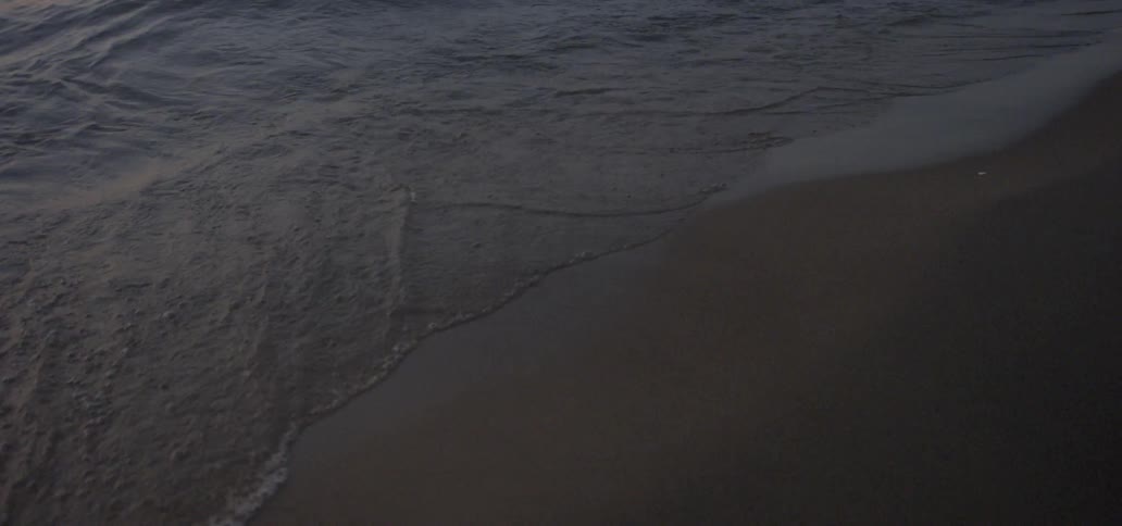 Ocean waves wash ashore a sandy beach at sunset