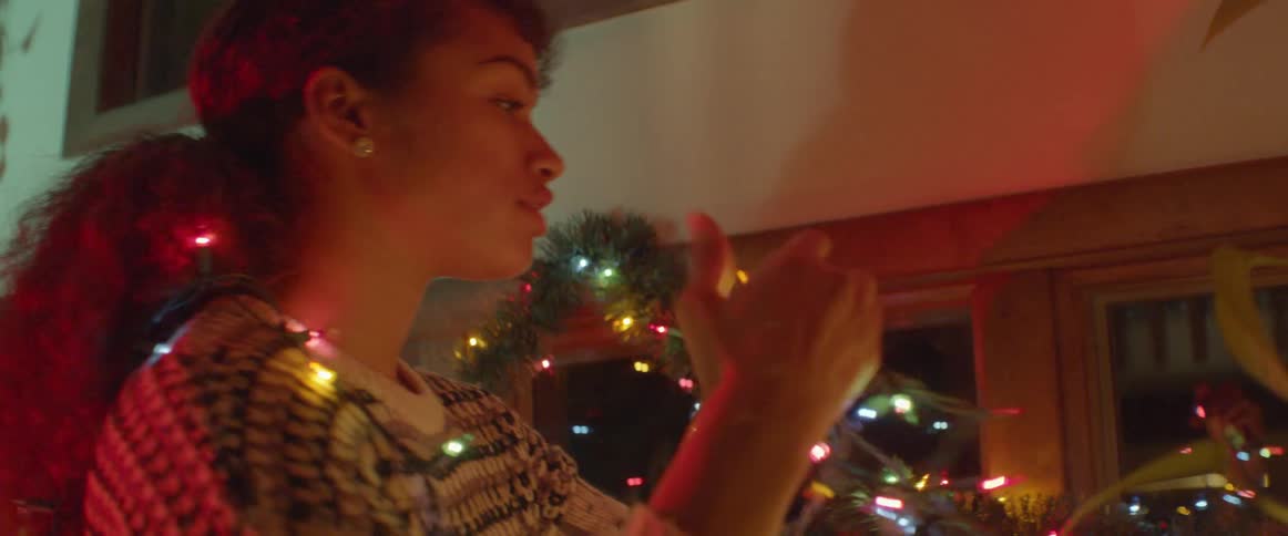 Woman wears a sweater as she hangs christmas lights around a window