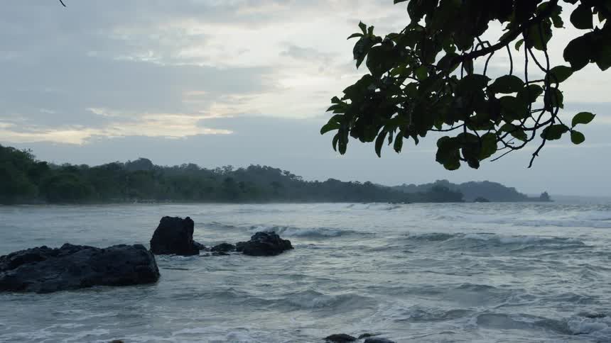 The rough water splashes against the rocks by the shore