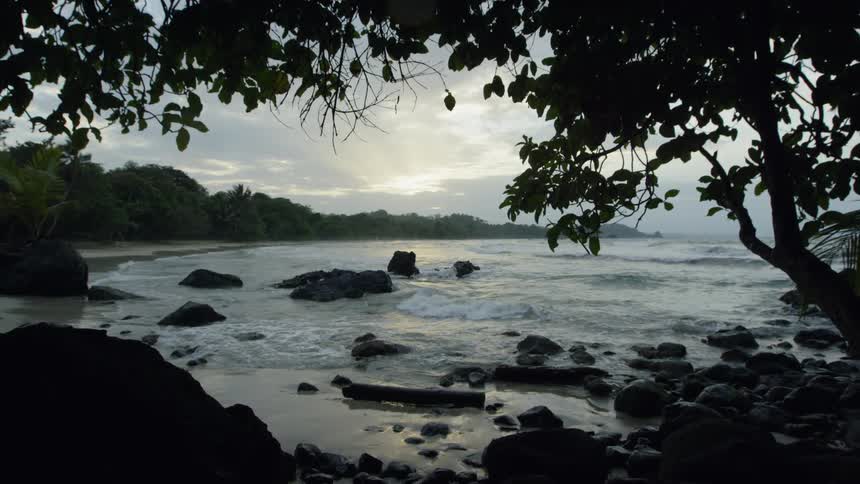 Waves crash around the rocks near the sandy shore