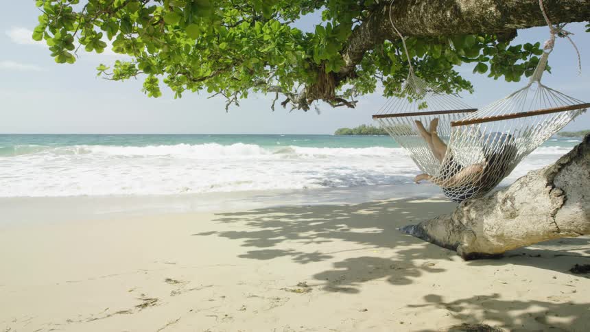 Woman relaxes in a hammock on a beach
