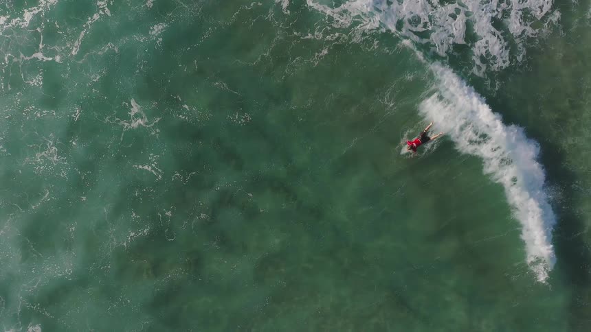 Waves roll over a man laying on a surfboard in the ocean