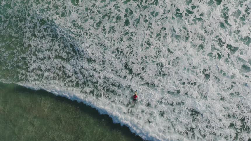 White frothy waves roll over a man on a surfboard in the ocean