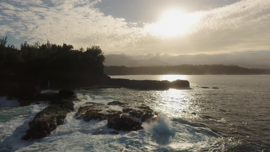 Waves crash into the rocks under the bright sun
