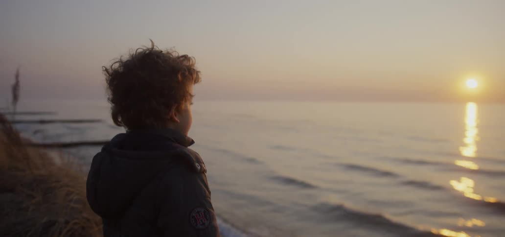 A boy stands on a beach at sunset