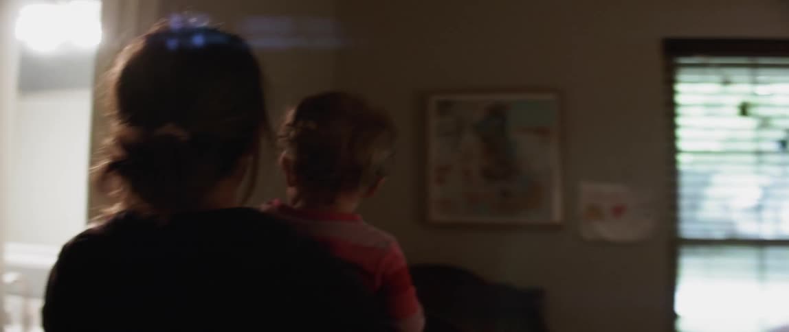 A woman carrying a baby walks into a room to shut off a light