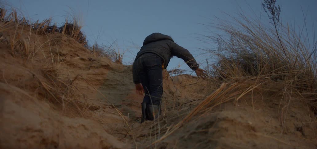 A boy climbs up a sandy hillside