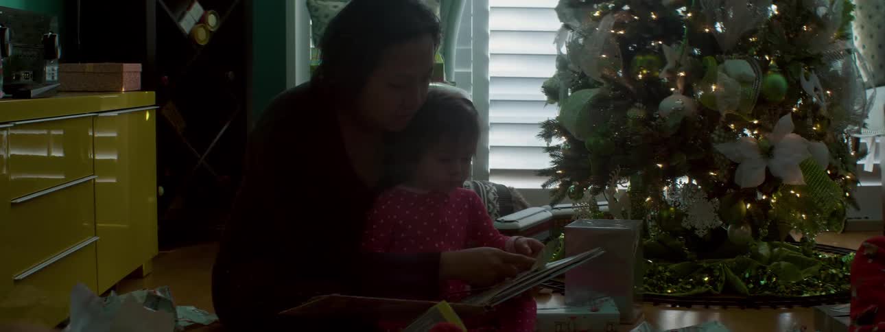 A woman reads a book with a young girl by the christmas tree