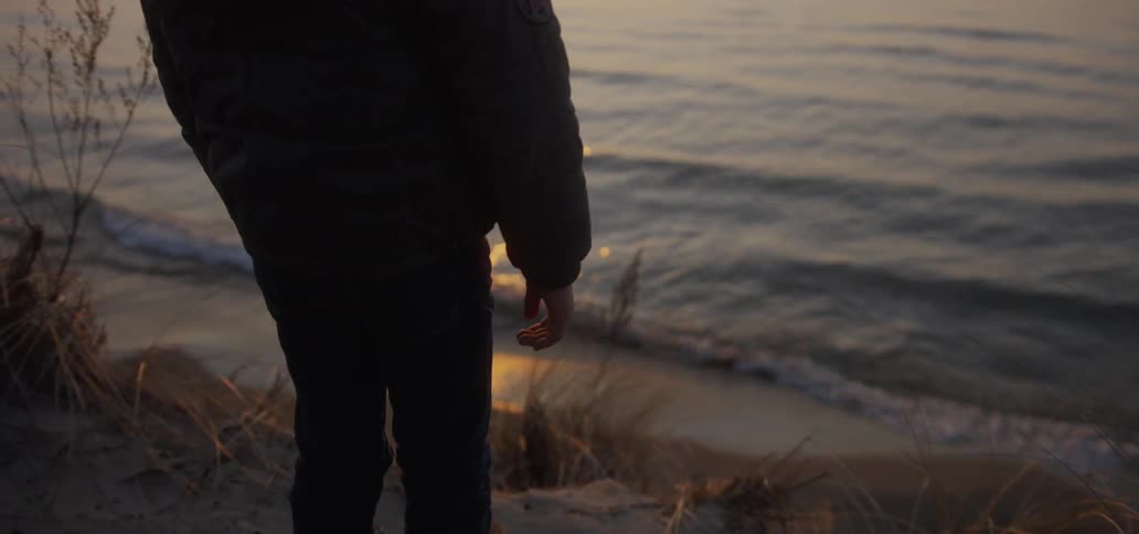 The person stands by the water at sunset