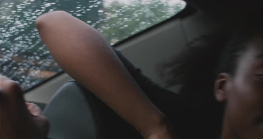 A young woman is looking out the window of a car on a rainy day