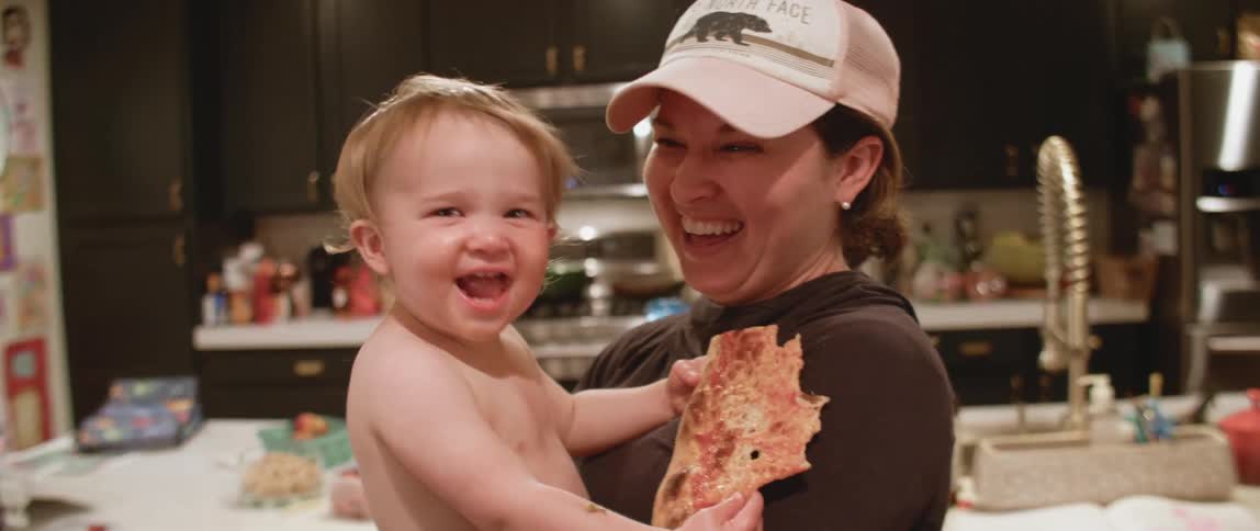 A woman holds a young baby eating pizza