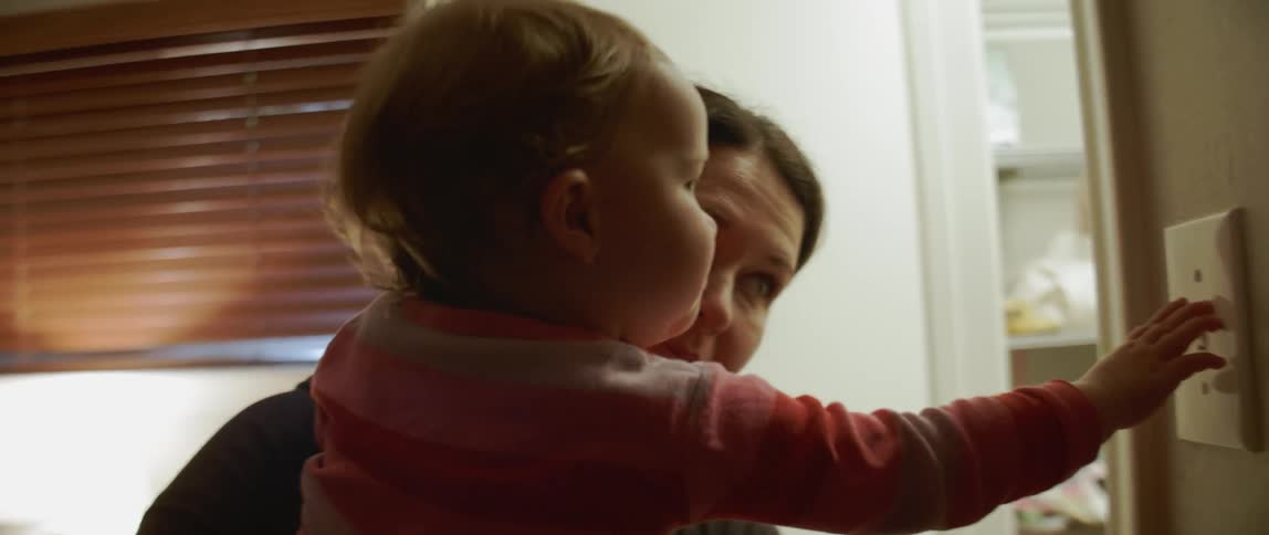 A mother is holding a baby and the baby is turning on and off a light