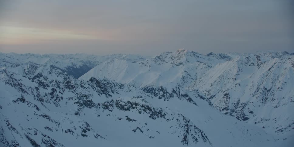 Snow covered mountains sit under a cloudy sky