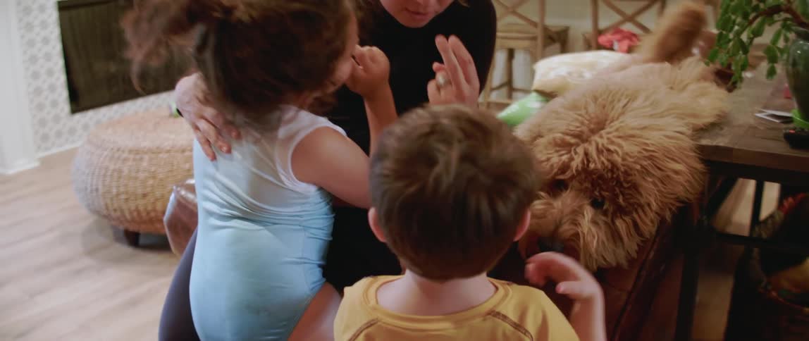 Woman plays with two children and a dog in the living room