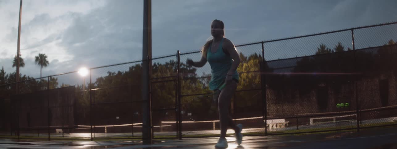 Woman plays tennis on an outdoor court at night