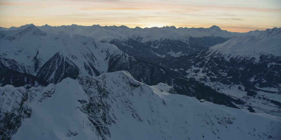 Sun sets behind snow covered mountains